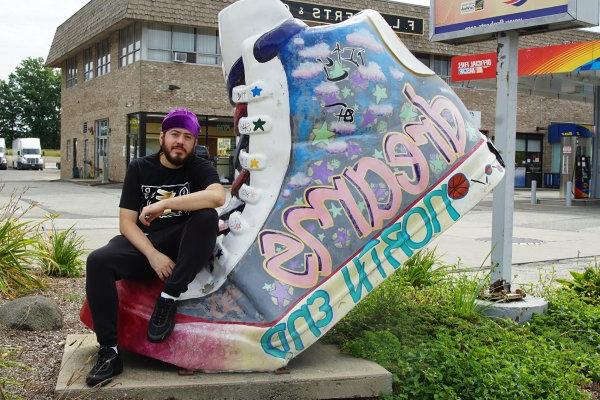 Samson Maldonado poses next to giant shoe with word "dreams" on it.